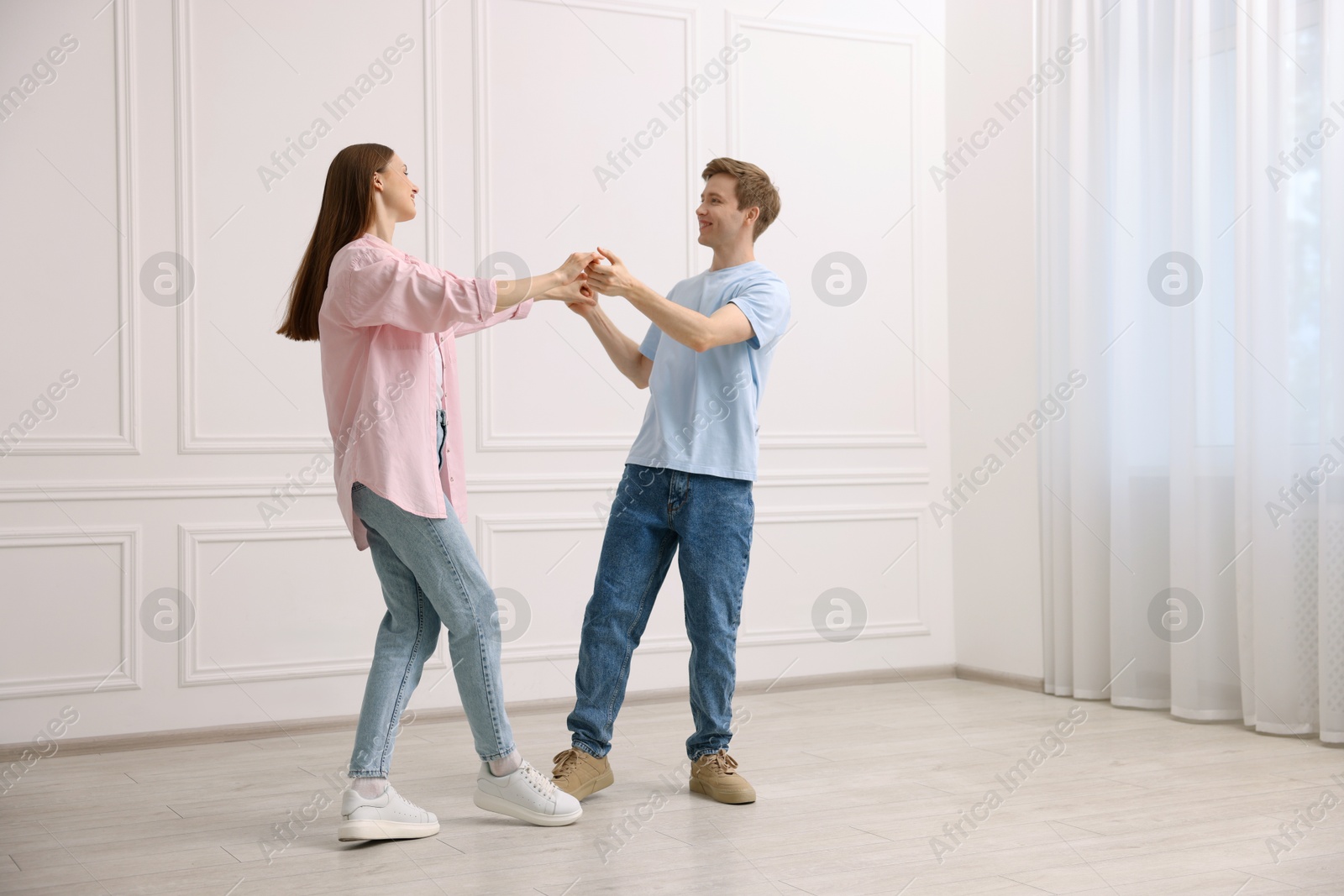 Photo of Happy couple dancing together near white wall at home