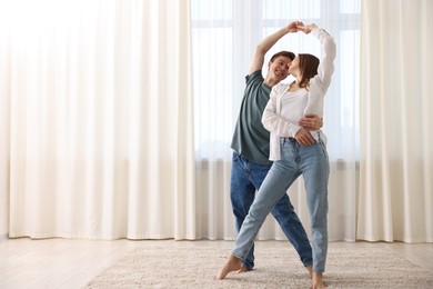 Photo of Happy young couple dancing together at home. Space for text