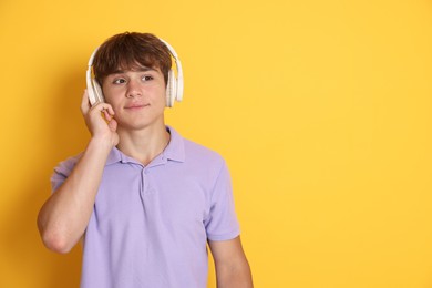 Photo of Cute teenage boy listening to music on yellow background. Space for text
