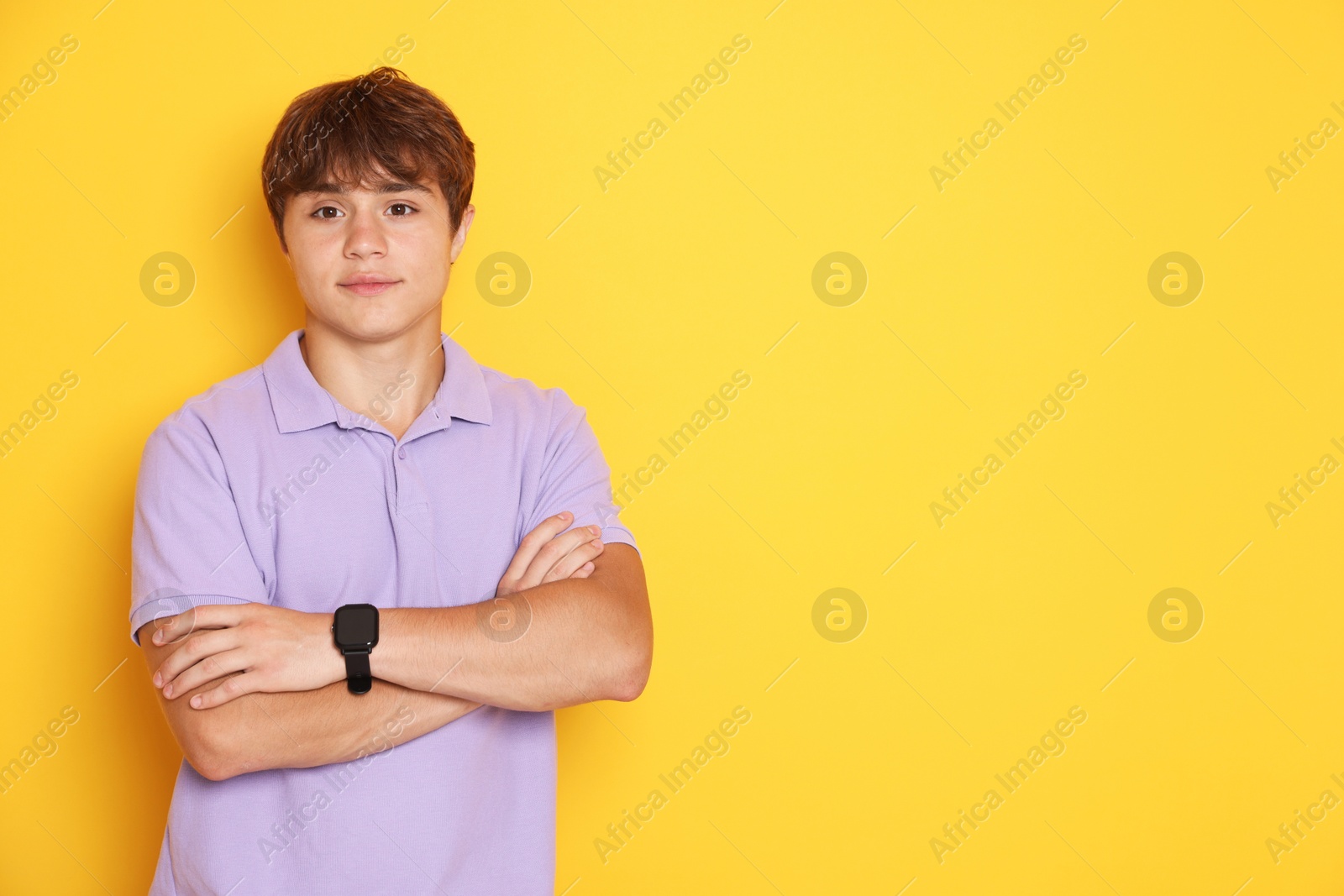 Photo of Cute teenage boy with crossed arms on yellow background. Space for text