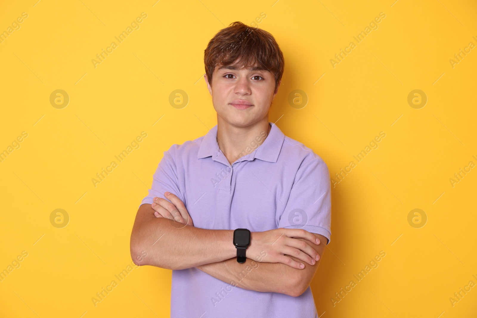 Cute teenage boy with crossed arms on yellow background Photo of Cute teenage boy with crossed arms on yellow background