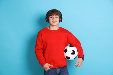 Photo of Smiling teenage boy in headphones with soccer ball on light blue background