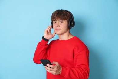 Photo of Cute teenage boy in headphones with smartphone on light blue background