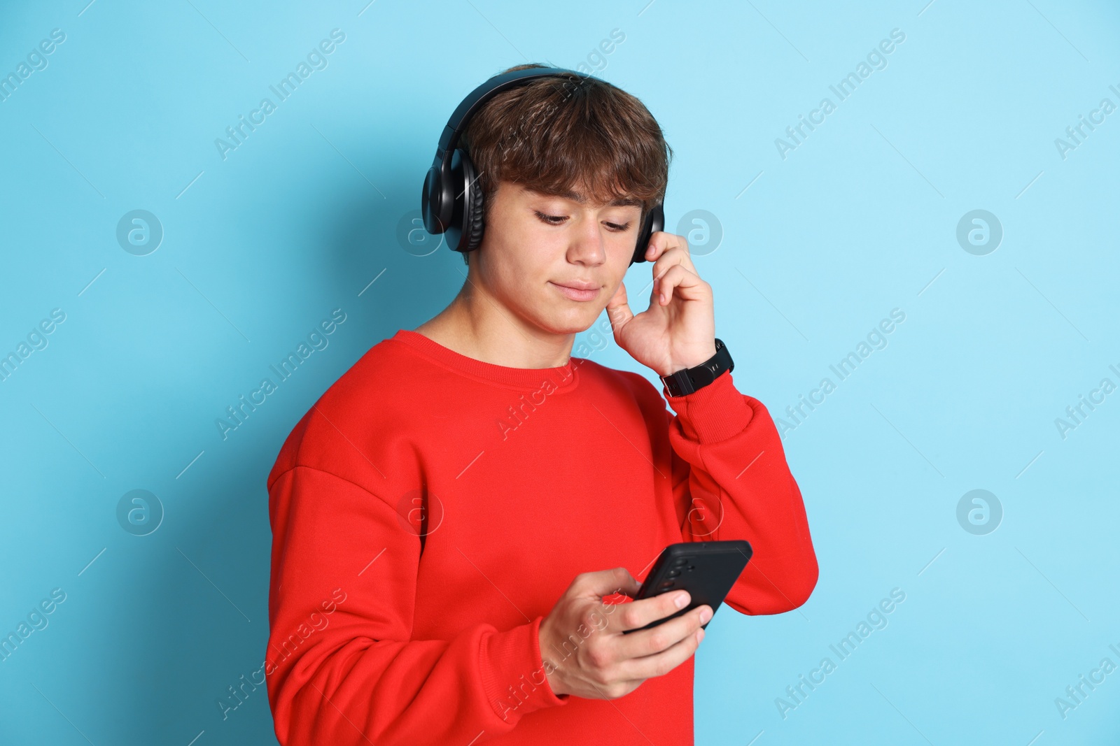 Cute teenage boy in headphones with smartphone on light blue background Photo of Cute teenage boy in headphones with smartphone on light blue background