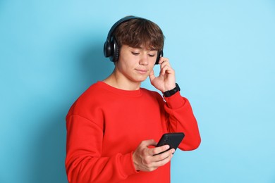 Photo of Cute teenage boy in headphones with smartphone on light blue background