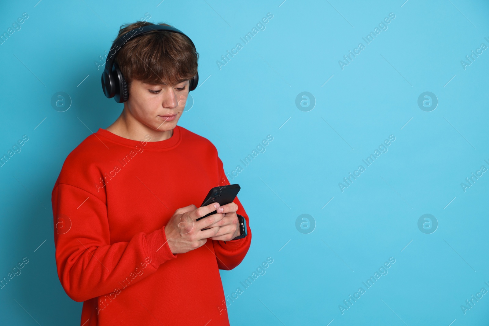 Photo of Cute teenage boy in headphones with smartphone on light blue background. Space for text