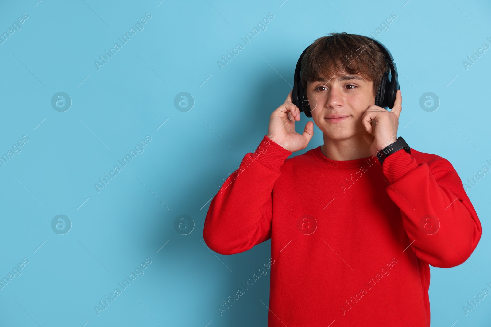 Cute teenage boy in headphones on light blue background. Space for text Photo of Cute teenage boy in headphones on light blue background. Space for text