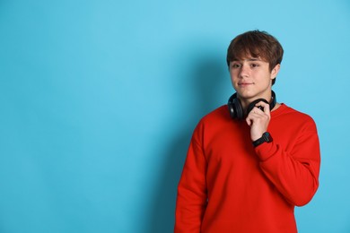 Photo of Cute teenage boy with headphones on light blue background. Space for text