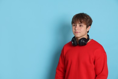 Photo of Cute teenage boy with headphones on light blue background. Space for text
