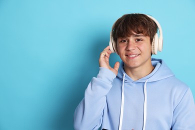 Photo of Portrait of smiling teenage boy in headphones on light blue background. Space for text