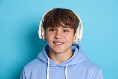 Photo of Portrait of smiling teenage boy in headphones on light blue background