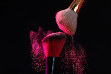 Photo of Makeup brushes with pink eye shadow on black background, closeup
