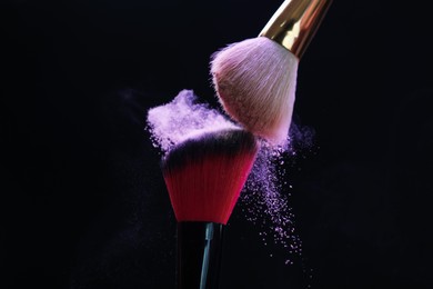 Photo of Makeup brushes with purple eye shadow on black background, closeup