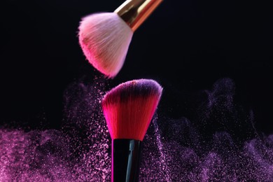 Photo of Makeup brushes with pink eye shadow on black background, closeup