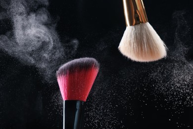 Photo of Makeup brushes with cosmetic powder on black background, closeup