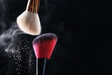 Photo of Makeup brushes with cosmetic powder on black background, closeup. Space for text