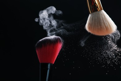 Photo of Makeup brushes with cosmetic powder on black background, closeup