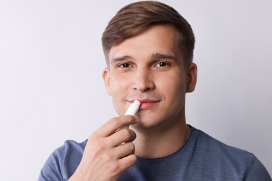 Photo of Young man applying lip balm onto his lips on light grey background