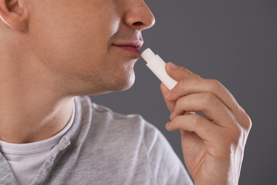 Photo of Young man applying lip balm onto his lips on grey background, closeup