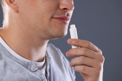 Photo of Young man applying lip balm onto his lips on grey background, closeup