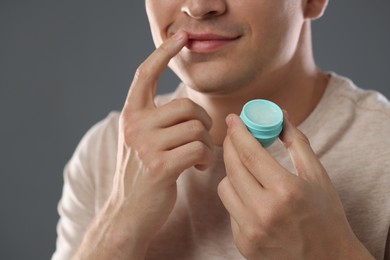 Photo of Young man applying lip balm onto his lips on grey background, closeup