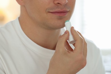 Photo of Young man applying lip balm onto his lips at home, closeup