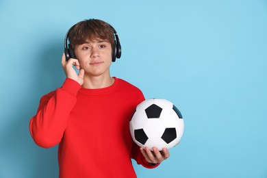 Photo of Cute teenage boy in headphones with soccer ball on light blue background. Space for text