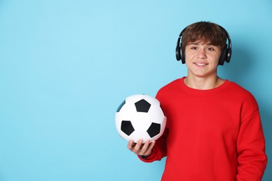 Photo of Portrait of smiling teenage boy in headphones with soccer ball on light blue background. Space for text