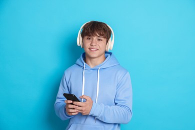 Photo of Smiling teenage boy in headphones with smartphone on light blue background