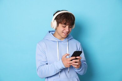 Photo of Smiling teenage boy in headphones with smartphone on light blue background