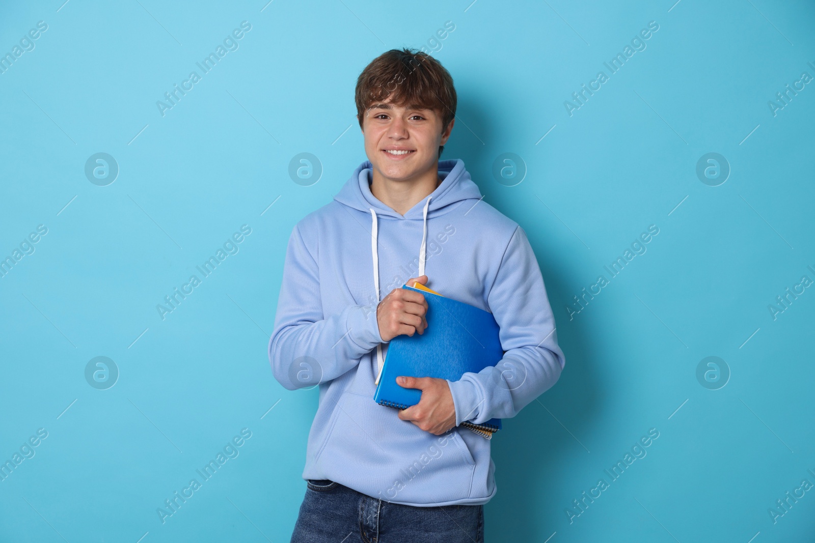 Photo of Portrait of smiling teenage boy with book on light blue background
