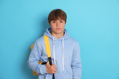 Photo of Portrait of cute teenage boy with backpack on light blue background
