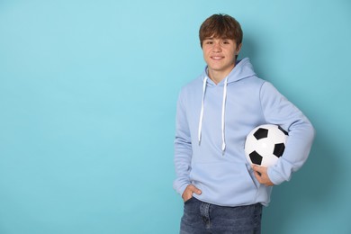 Photo of Portrait of smiling teenage boy with soccer ball on light blue background. Space for text