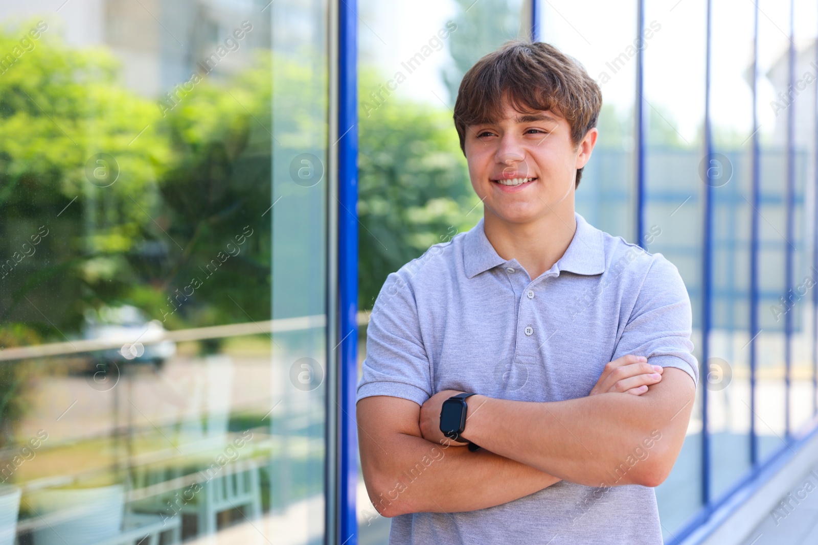 Photo of Smiling teenage boy with crossed arms near building outdoors