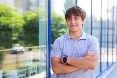 Photo of Smiling teenage boy with crossed arms near building outdoors