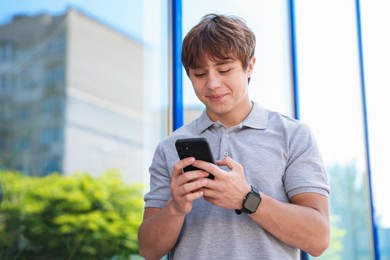 Photo of Cute teenage boy with smartphone near building outdoors