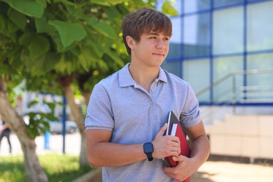 Photo of Cute teenage boy with books on city street