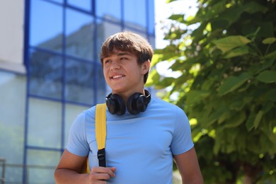 Photo of Smiling teenage boy with headphones on city street, low angle view