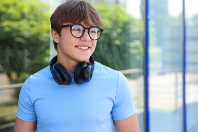Photo of Smiling teenage boy in glasses with headphones near building outdoors