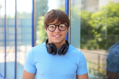 Photo of Portrait of smiling teenage boy in glasses with headphones near building outdoors
