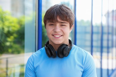 Photo of Smiling teenage boy with headphones near building outdoors