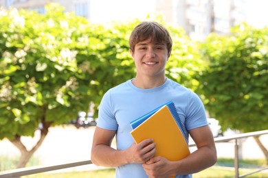 Photo of Portrait of smiling teenage boy with notepads on city street