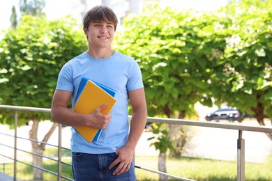 Photo of Smiling teenage boy with notepads on city street
