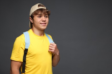 Photo of Smiling teenage boy in baseball hat with backpack on grey background. Space for text