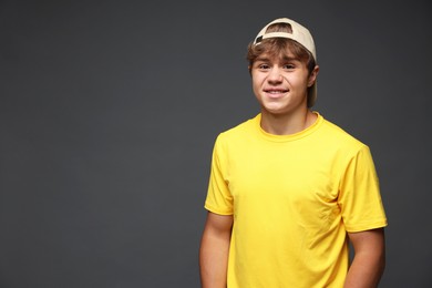 Photo of Portrait of smiling teenage boy in baseball hat on grey background. Space for text