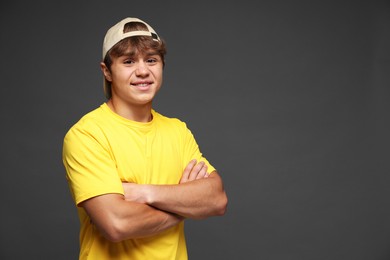 Photo of Portrait of smiling teenage boy in baseball hat with crossed arms on grey background. Space for text