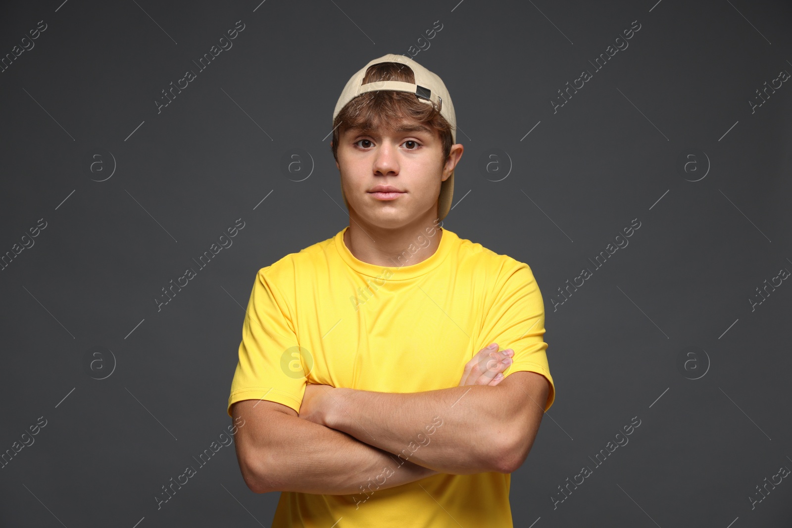 Portrait of cute teenage boy in baseball hat with crossed arms on grey background Photo of Portrait of cute teenage boy in baseball hat with crossed arms on grey background