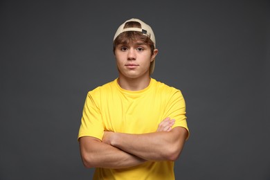 Photo of Portrait of cute teenage boy in baseball hat with crossed arms on grey background