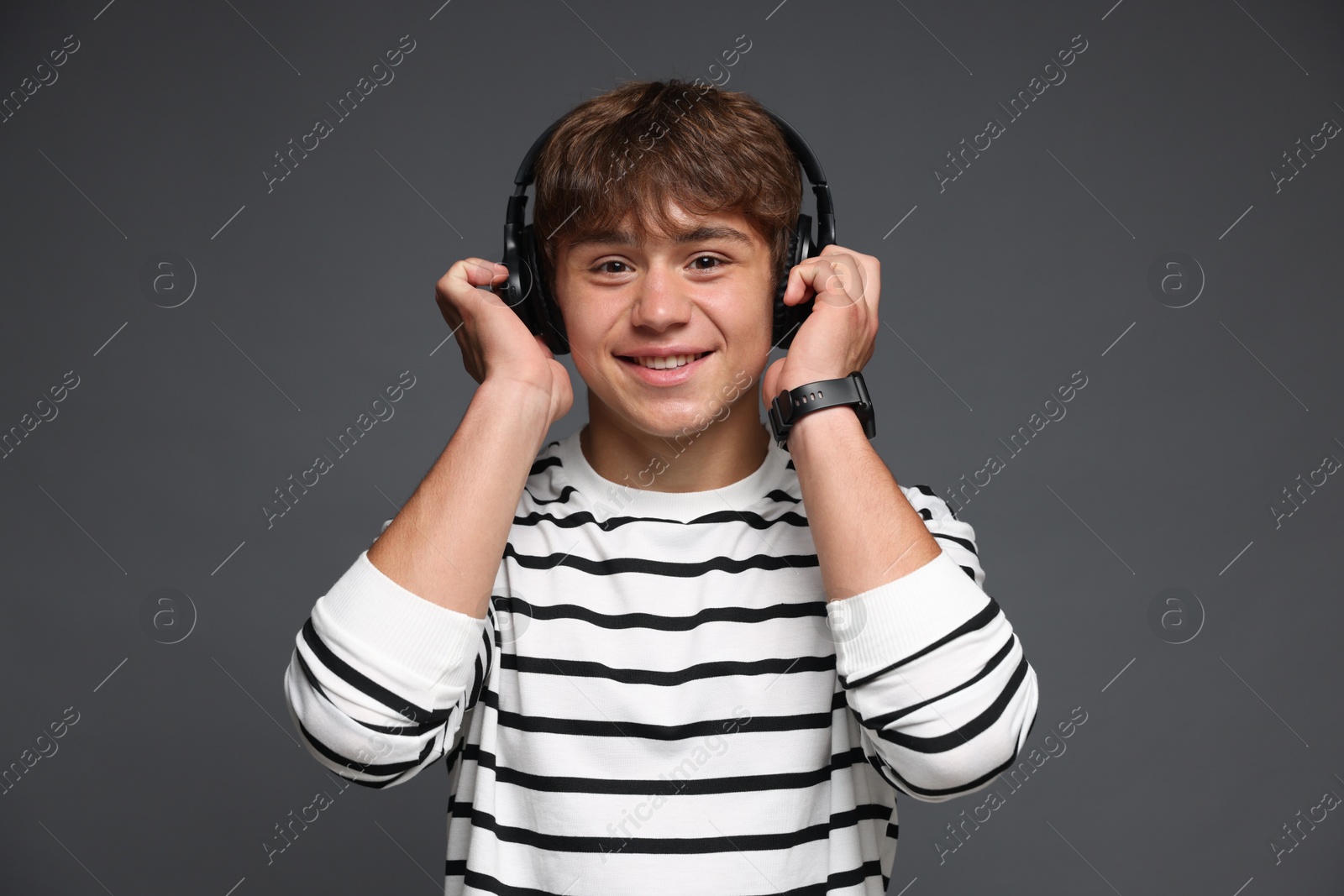 Photo of Portrait of smiling teenage boy in headphones on grey background