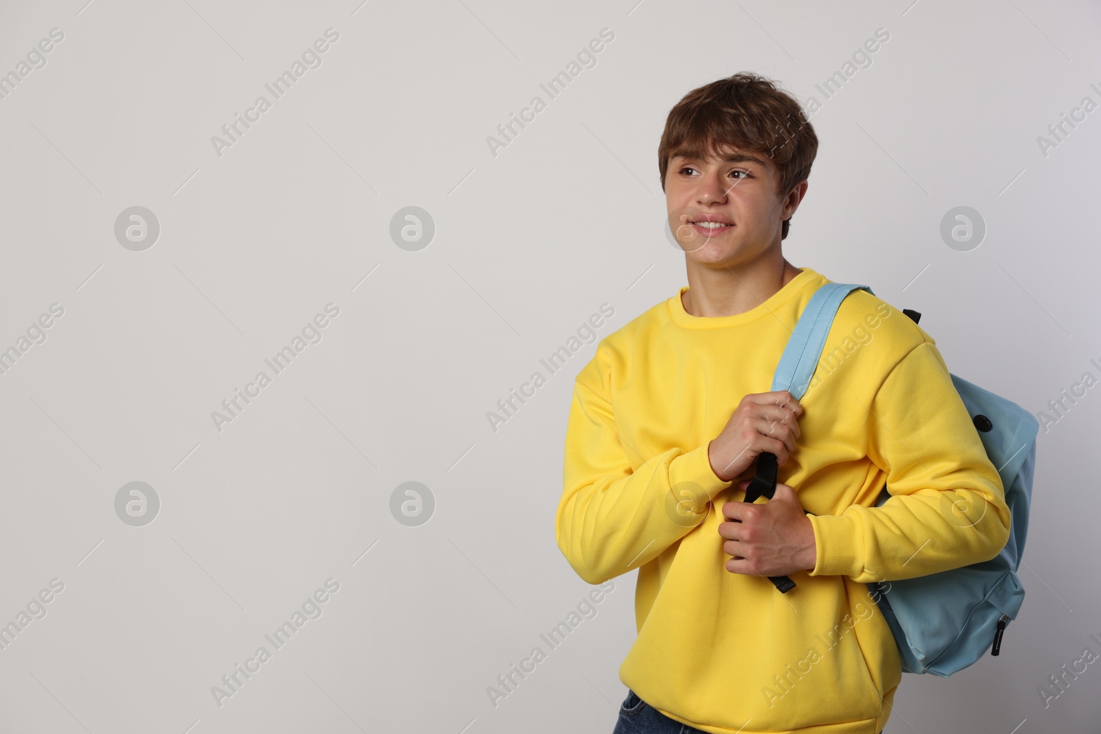 Photo of Smiling teenage boy with backpack on light grey background. Space for text